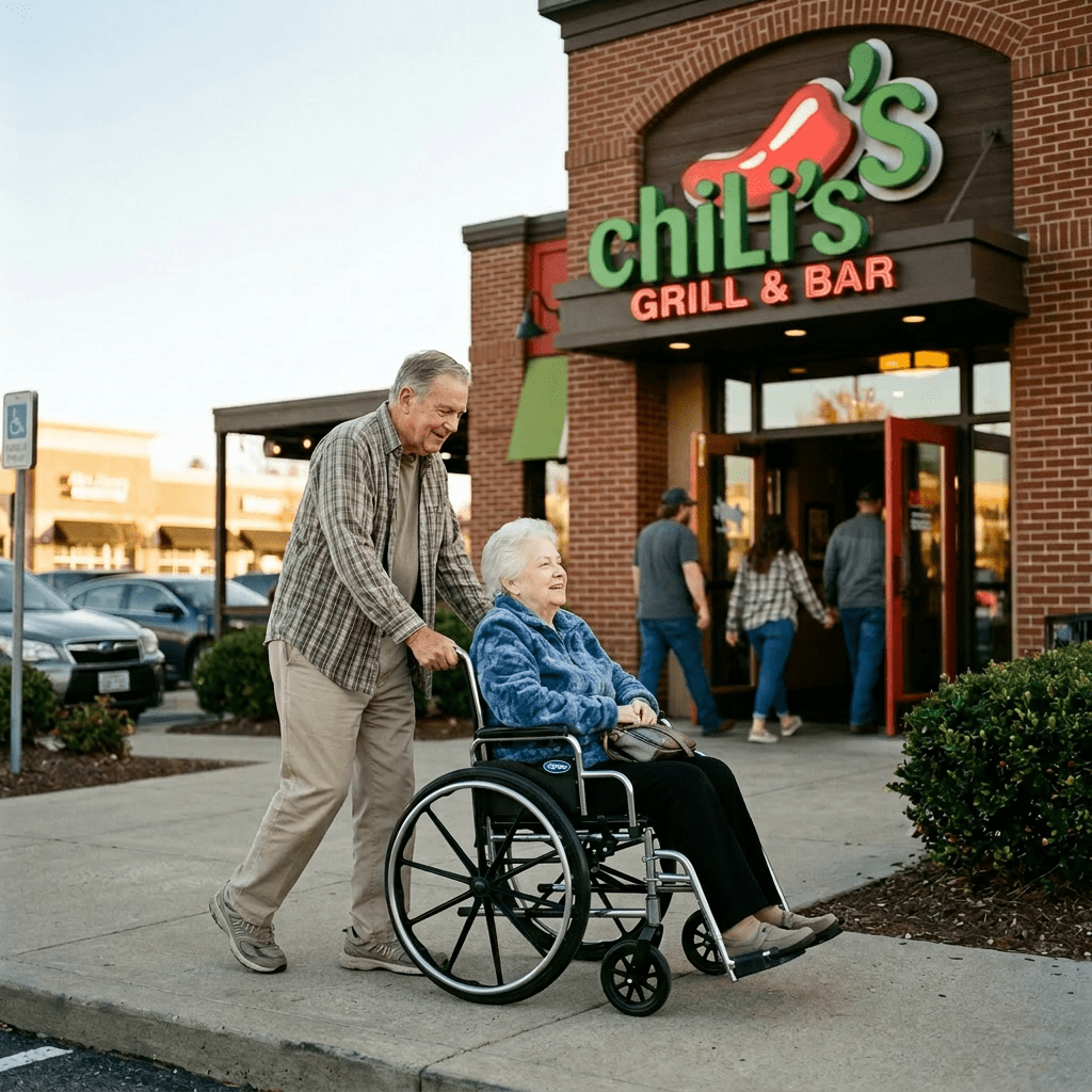 Elderly man pushing a woman in a wheelchair outside Chili's restaurant